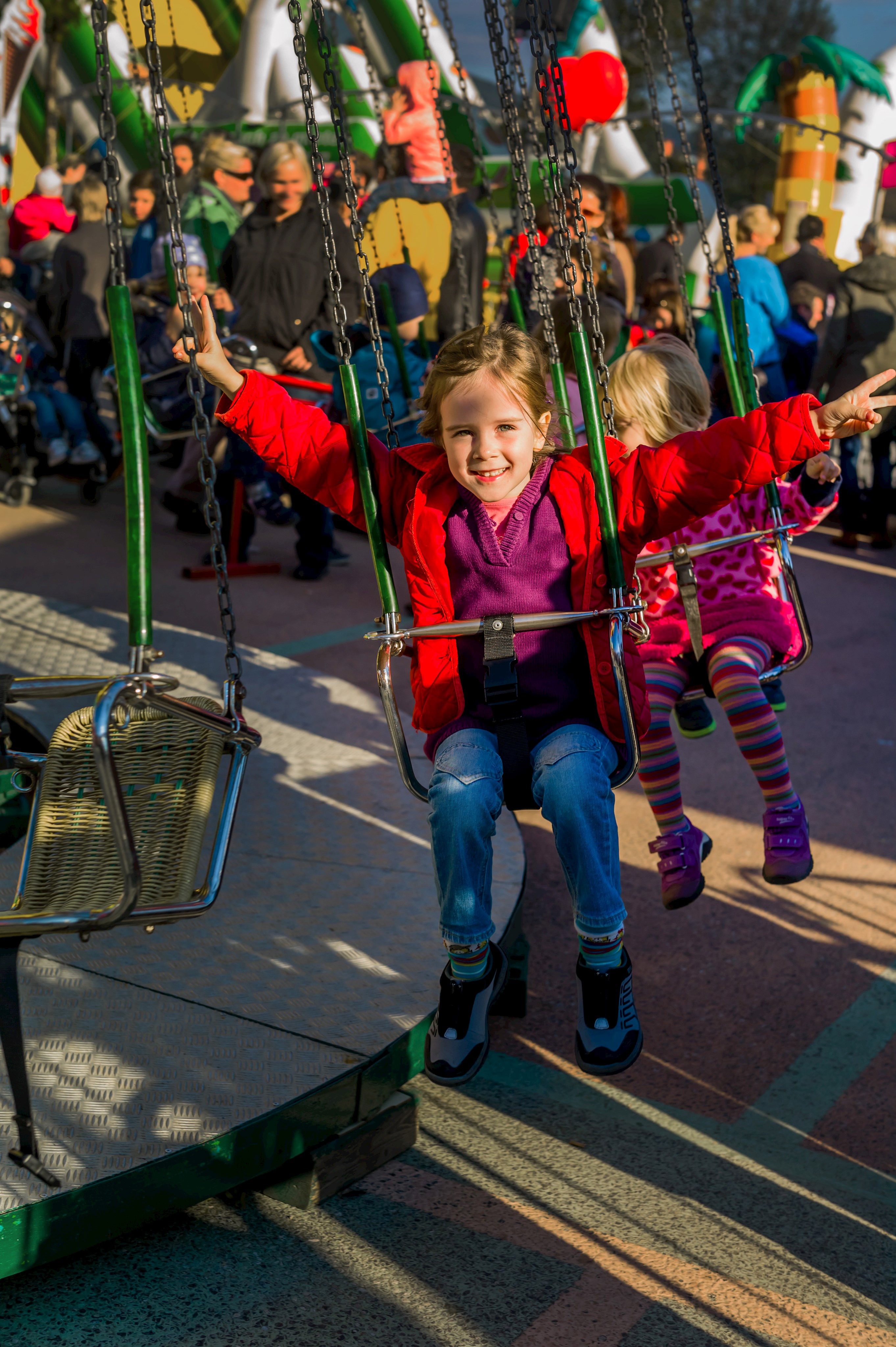 Kinder im Kettenkarussel mit Eltern im Hintergrund