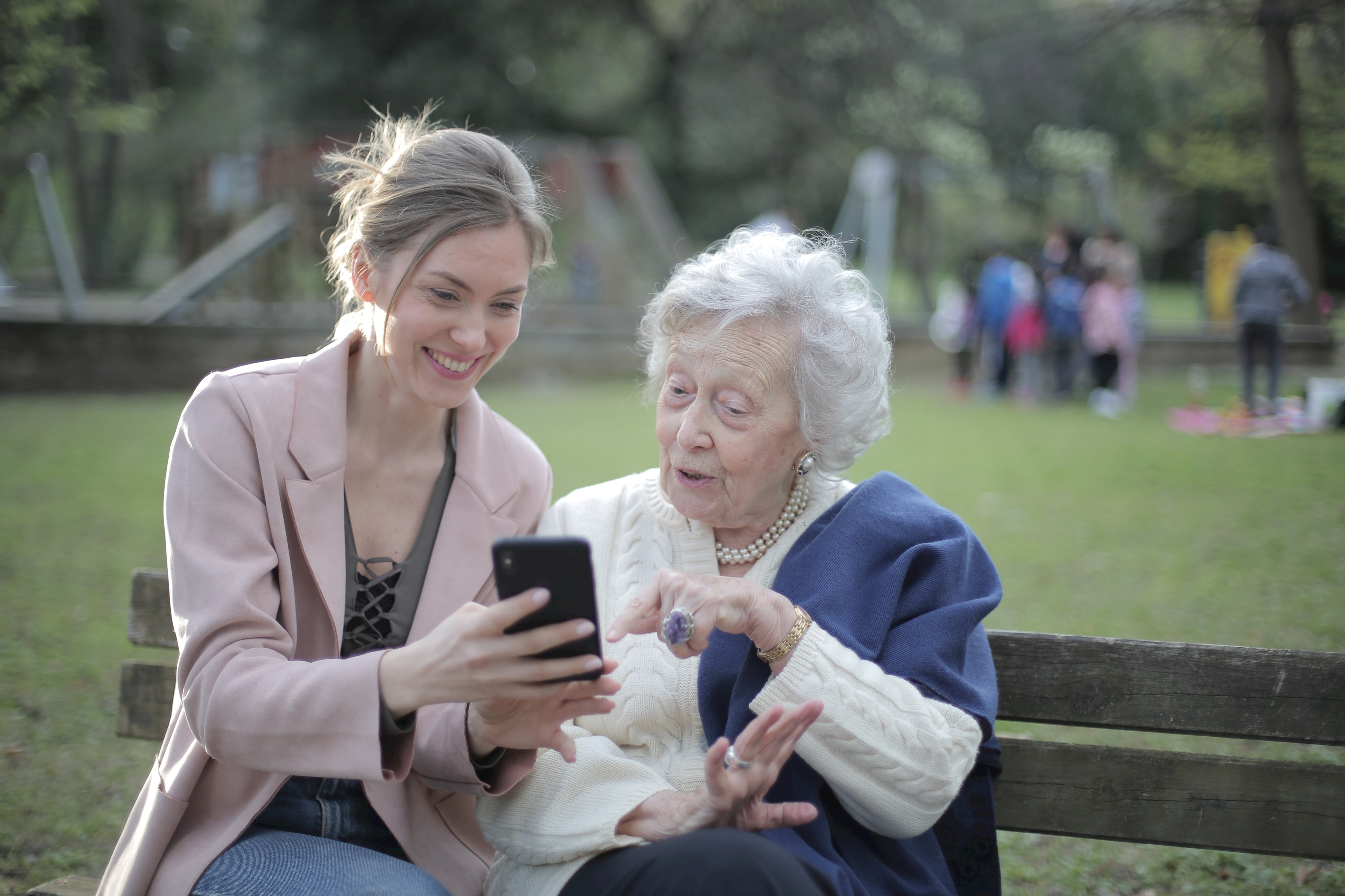 Junge Frau zeigt ältere Dame etwas auf dem Smartphone