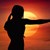 Silhouette einer Frau steht mit ausgestrecktem Arm vor gelber Sonne